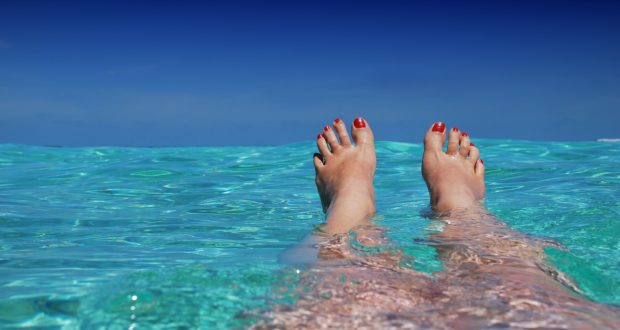benen en roodgelakte voeten in een azuur blauw zee